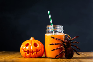 Halloween pumpkin with carrot juice in masons jar on black background