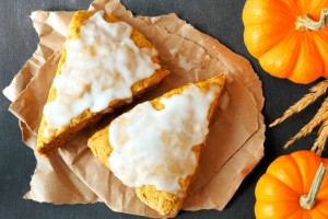 Sweet autumn pumpkin scones with frosting, overhead view on dark slate background